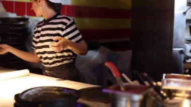 Kadın aşçı pizza hamuru hazırlamaya odaklanıyor. Londra 'daki hareketli bir restoran mutfağında merdaneyi ustalıkla kullanıyor. Mutfak işçiliği sanatını ön plana çıkarıyor.