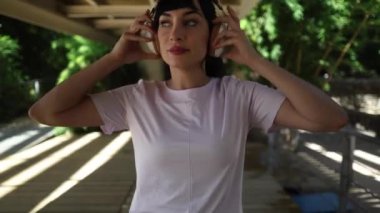 Koşmaya hazırlanan bayan sporcu, kulaklık takıyor ve müziğe başlıyor. Gündüz vakti şehir köprüsü altında güneş ışığı ve gölgelerle koşu yaparken.