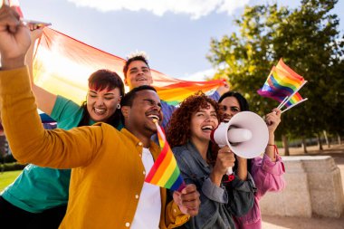 Bir grup neşeli, çoklu etnik aktivist ellerinde gökkuşağı bayrakları ve megafonla yaz boyunca canlı bir halk parkında lgbtq artı hakları protesto ediyorlar.