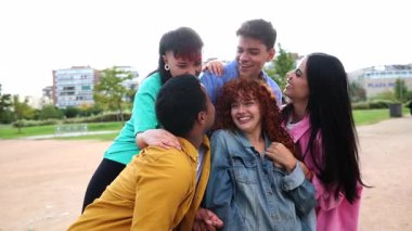 Genç arkadaşlar sıcak bir bağ anı paylaşıyorlar, güneşli bir sonbahar gününde şehir parkında kucaklaşıp gülüyorlar, gerçek mutluluğu ve farklı arkadaşlıkları gösteriyorlar.