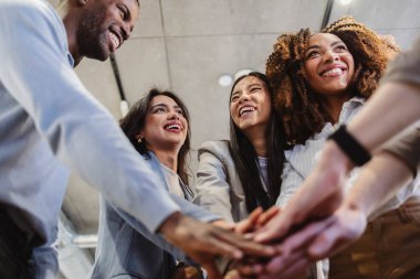 Çeşitli güler yüzlü iş adamları ofiste el ele tutuşup başarılarını kutluyor ve güçlü bir takım çalışması sergiliyorlar.