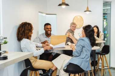 Çok ırklı iş adamları, çağdaş bir ofis ortamında birlikte çalışırken üretken bir toplantı yaparak fikir ve stratejileri tartışıyor.