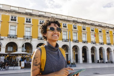 Güneş gözlüğü ve sırt çantası takan genç bir bayan turist güneşli bir günde Lizbon 'un şehir merkezinde olduğunu keşfederken tabletindeki haritaya danışıyor.