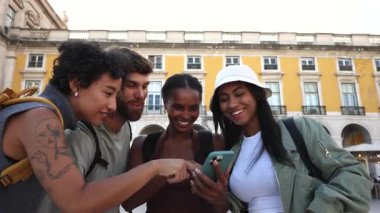 Gezmek için akıllı telefonu kullanan, Lizbon, Portekiz 'deki tarihi comercio meydanını güneşli yaz günlerinde keşfederken neşeli anlar paylaşan çeşitli genç gezginler.