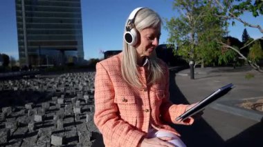 Olgun profesyonel müzik, uzaktan tablet üzerinde çalışırken, güneşli şehir parkında rahatça otururken, modern iş dengesi ve dijital bağlantıyı somutlaştırıyor.