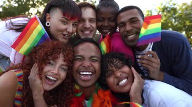 Çok ırklı lgbtqia artı arkadaşlar gökkuşağı bayrakları sallarken sevinç saçıyorlar, canlı park ortamında gurur ve birliği kutluyorlar gerçek gülümsemelerle ve mutluluğu paylaşıyorlar.