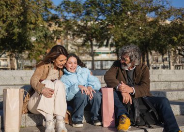 Gülümseyen ebeveynler, güneşli bir günün keyfini çıkardıktan sonra şehir merkezindeki merdivenlerde dinlenirken kızlarına sarılıyorlar.