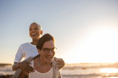 Kaygısız çoklu etnik çiftler gün batımında sahilde oynaşıp eğleniyorlar. Birlikte gülüyorlar ve okyanus kıyısındaki yaz tatillerinde keyifli anları paylaşıyorlar.