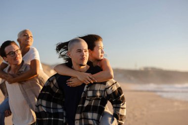 İki adam, gün batımında kumsaldaki kadın arkadaşlarına sırtına binip gülücükler ve kahkahalarla dolu tasasız bir tatil boyunca dostluk ve neşeyi kutluyorlar.