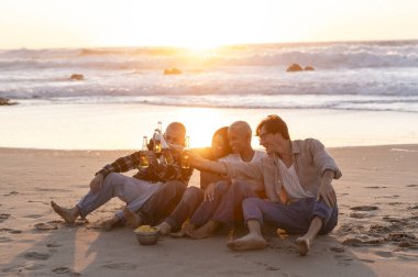 Beş arkadaş kumlu sahilde oturmuş, içkilerini yudumluyor ve muhteşem altın saat günbatımında sırılsıklam oluyorlar, kahkaha ve beraberlikle dolu neşeli anılar yaratıyorlar.