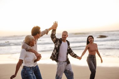 Dört mutlu arkadaş gün batımında kumsalda rahatlatıcı bir yürüyüşün tadını çıkarıyor, beşlik çakıyor ve el ele tutuşuyorlar, arkadaşlıklarını ve güzel manzaralarını kutluyorlar.