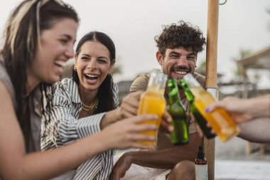 Neşeli genç arkadaşlar şişelerce ferahlatıcı içeceklerle kadeh kaldırıyor, neşeli bir plaj partisinde gülüyor ve eğleniyorlar, birlikte unutulmaz yaz anıları yaratıyorlar.