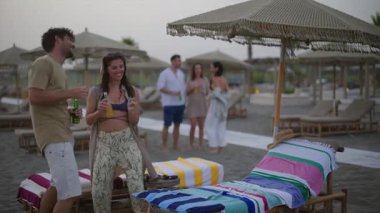 Genç turistler kumlu sahilde kaygısız bir akşamın tadını çıkarıyorlar, dans ediyorlar, renkli şemsiyeler altında içiyorlar, yaz tatilini arkadaşlarıyla birlikte altın gün batımında kutluyorlar.