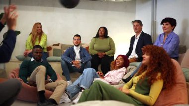 Bir grup farklı ofis çalışanı rahatlıyor, dinlenme odasında kaynaşıyor, top oynarken iş arkadaşlığı ve takım bağlantısının keyfini çıkarıyor.