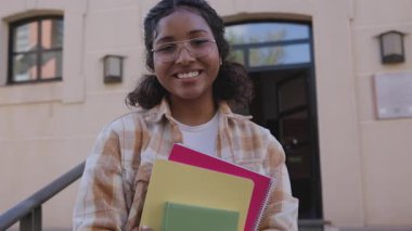 Afrika kökenli Amerikalı öğrenci, elinde renkli defterler, akademik coşku ve gelecekteki başarılarıyla güvenle okulun girişinde duruyor.