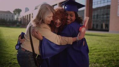 Mavi elbiseli gururlu mezunlar annelerine sarılıp akademik başarılarını ellerinde diplomalarla üniversitenin kampüs bahçesinde kutluyorlar.
