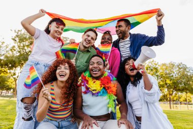 Neşeli çok ırklı lgbtq grubu artı gökkuşağı bayrakları ve megafon taşıyan aktivistler, halka açık bir parkta gey gururunu kutluyorlar, çeşitliliği ve dahil edilmeyi destekliyorlar.