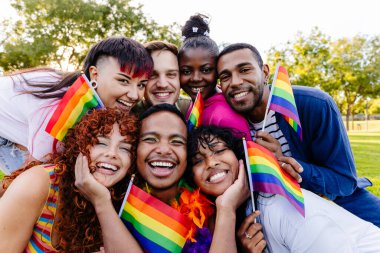 Neşeli, çoklu etnik arkadaşlar birlikte gülüp kucaklaşırken güneşli bir parkta neşeli bir gay onur etkinliğinde gururla küçük gökkuşağı bayrakları tutarken aşkı ve birliği kutluyorlar.