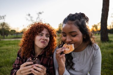 İki genç kadın gün batımında parkta tatlı bir ziyafetin tadını çıkarırken aynı zamanda sevgi dolu bir arkadaşlık anı yaratıyorlar.