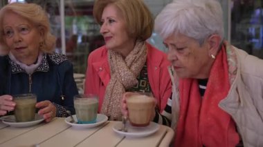 İki yaşlı kadın açık bir kafede oturup kahvelerini yudumluyor ve keyifli sohbetler ediyor. Rahatlama ve arkadaşlığın tadını çıkarıyorlar.