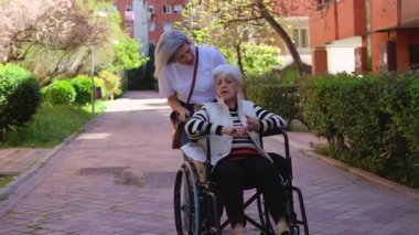 Kendini adamış hemşire, dışarıda rehabilitasyon egzersizleri yapan, iyileşme ve hareketliliği teşvik eden tekerlekli sandalyede oturan yaşlı bir kadına destek ve rehberlik eder.