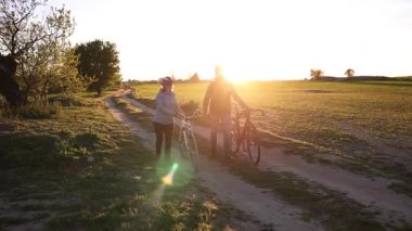 Romantik çift gün batımında huzurlu köy yolunda bisiklet yürüyüşünden keyif alıyor, doğanın sakinliğini ve altın ışığını kucaklıyor.
