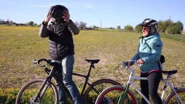 Olgun bisikletçiler kırsal bisiklet sürmeye hazırlanıyor, koruyucu kasklar takıyor ve güneşli bir günde yemyeşil alanda pedal çevirmeden önce beklenti anlarını paylaşıyorlar.