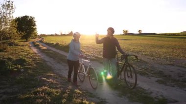 Mutlu çift gün batımında pikoresk bir kır yolunda bisikletleriyle yürüyor, altın saat ışığının tadını çıkarıyor ve boş vakitlerini paylaşıyorlar.