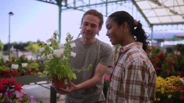 Gülümseyen çok ırklı bir çift bahçe merkezinden el değmemiş beyaz çiçekleri seçiyor, güzel bir koku soluyor ve samimi bir anı paylaşıyorlar.