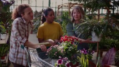 Çiçekçiyle bitki seçimini tartışan dost canlısı müşteriler renkli bahçe merkezinde alışveriş arabalarını iterek bahçıvanlık için ortak coşkularını dile getiriyorlar.