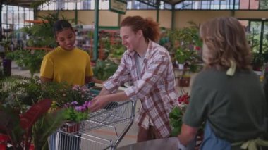Dost canlısı kasiyer, müşterilere canlı bitkiler seçmede ve bahçe kasasında perakende işlemlerini tamamlamalarında yardımcı oluyor.