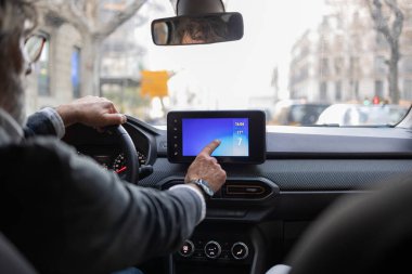 Olgun iş adamı şehirde araba sürüyor ve dokunmatik ekranlı GPS navigasyon sistemini kullanıyor, işe giderken modern teknolojinin tadını çıkarıyor.