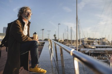 Hayatı düşünürken, sırt çantalı yaşlı bir adam marinada yeniden kullanılabilir bir bardaktan içmeyi sever. Gün batımında gökyüzünü ılık renklerle boyarken yelkenlilerin süzülüşüne hayran kalır.
