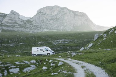 Durmitor Ulusal Parkı 'ndaki geniş dağ manzarasının sükunetini kucaklayan, çimenli bir arazide park etmiş beyaz bir karavan, mongol, sakin bir sabah boyunca...