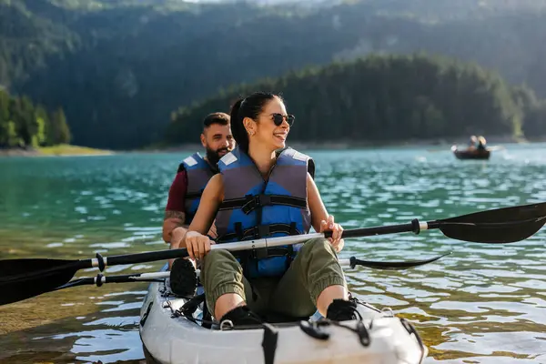 Can yelekleri giyen turistler, huzurlu bir dağ gölünde şişme bir kanoya binip yaz tatillerinde doğanın huzur ve güzelliğinin tadını çıkarıyorlar.