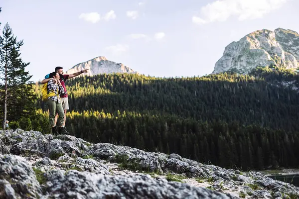 İki yürüyüşçü, kayalık bir çıkıntının üzerinde duruyor. Uçsuz bucaksız, yemyeşil bir ormanı seyrederken nefes kesen manzarayı kucaklıyorlar. Huzurlu bir gökyüzünün altındaki yüksek dağ zirvelerine çıkıyorlar.