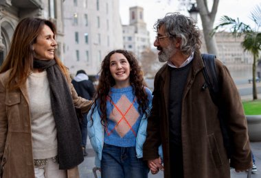 Gülümseyen ebeveynler kızlarıyla el ele tutuşup canlı bir şehirde dolaşırken, aile tatili maceraları boyunca neşe ve beraberlik anlarını sevgiyle anarlar.