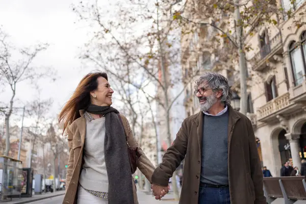 Neşeli son sınıf çifti el ele tutuşup gülerken canlı bir şehir caddesinde emekliliklerini kucaklıyor ve neşeyle dolu aktif bir şehir hayatının tadını çıkarıyor.