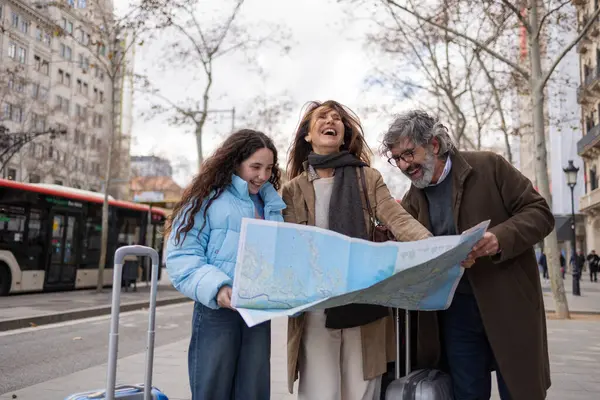 Gülümseyen turist ailesi hareketli bir şehir caddesinde haritaya danışıyor, bavullarını tutuyor ve bir sonraki heyecan verici varış noktalarını planlarken kahkahalarını paylaşıyorlar.