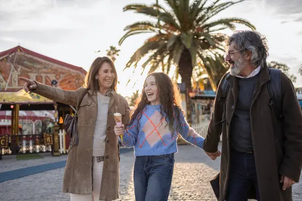 Gülümseyen büyükanneler ve büyükbabalar neşeli torunlarıyla el ele tutuşurken, bir lunaparkta yürüyüş yaparken kız dondurma yiyor ve büyükanne de ilginç bir şeye işaret ediyor.