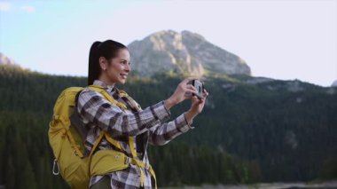 Dişi sırt çantalı gezgin akıllı telefonlu manzaralı dağ manzarası yakalıyor, tek başına yürüyüş yaparken huzurlu doğayı deneyimliyor, maceracı ve neşeli açık hava yaşam tarzını somutlaştırıyor.