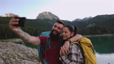 Mutlu yürüyüşçüler, akıllı telefonlarıyla dağ gölünün kenarındaki fotoğraflarına bakıp neşe ve bağlantı anlarının tadını çıkarıyorlar.