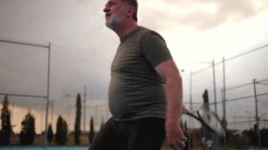 Olgun erkek atlet, güçlü tenis antrenmanlarını mavi sahada yapıyor. Açık hava sporları eğitimi sırasında kesin ve kararlı hareketler sergiliyor.