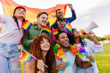 Çok ırklı lgbtq grubu artı aktivistler ve destekçiler neşeli bir şekilde bir parkta gay gururunu kutluyorlar, ellerinde canlı gökkuşağı bayrakları ve bir megafon, sevgi ve eşitlik mesajları yayıyorlar.