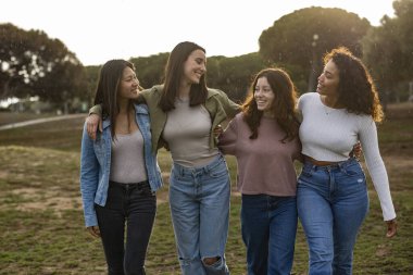 Dört farklı genç kadın, kollarını birbirlerine dolayarak parkta yürüyorlar, temiz havanın, hafif yağmurun ve arkadaşlarının arkadaşlarıyla birlikte olmanın tadını çıkarıyorlar.