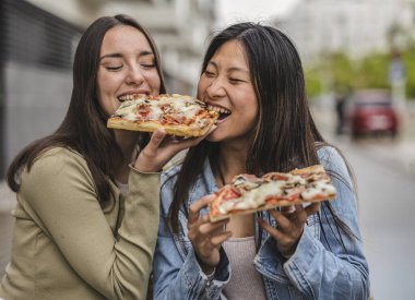 Şehirdeki sıradan bir günde pizza yerken eğlenen iki gülümseyen genç kadın arkadaşlıklarını kutluyor ve lezzetli fast food 'un tadını çıkarıyorlar.