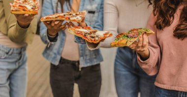 Dört arkadaş çeşitli pizza dilimlerinin tadını çıkarıyorlar. Lezzetli malzemeler ve tatlarla dolu sıradan bir yemek eşliğinde kahkaha ve sohbet paylaşıyorlar. Birlikte neşeli bir atmosfer yaratıyorlar.
