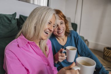 Parlak oturma odalarında rahat bir kanepede oturan, kahkahalarla kahkahaları paylaşan ve neşeli dostluk anları yaratan iki neşeli son sınıf kadını.