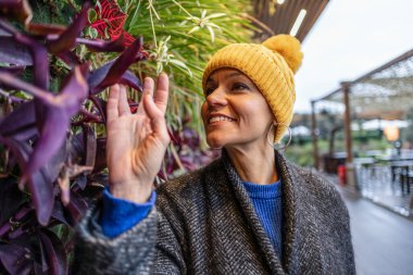 Gülümseyen kadın botanikçi dikey bir bahçede gelişen egzotik bitkilere nazikçe dokunuyor ve hayranlık duyuyor, yeşil alanlarla dolu canlı bir kamusal alanda yaptığı işten keyif alıyor.