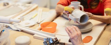 İki çömlekçi çömlek atölyesi sırasında seramik sanatının ve becerilerinin sergilendiği çeşitli alet ve malzemelerle çevrili bir çömlekçiyi süngerle düzleştiriyor ve bitiriyor.